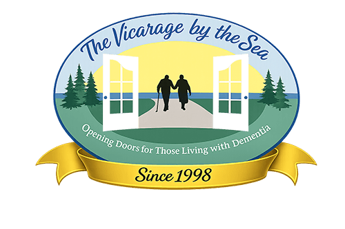 Logo for “The Vicarage by the Sea” showing two people holding hands, walking through open doors toward the sea, with trees and a yellow sunrise; text reads “Since 1998.”.